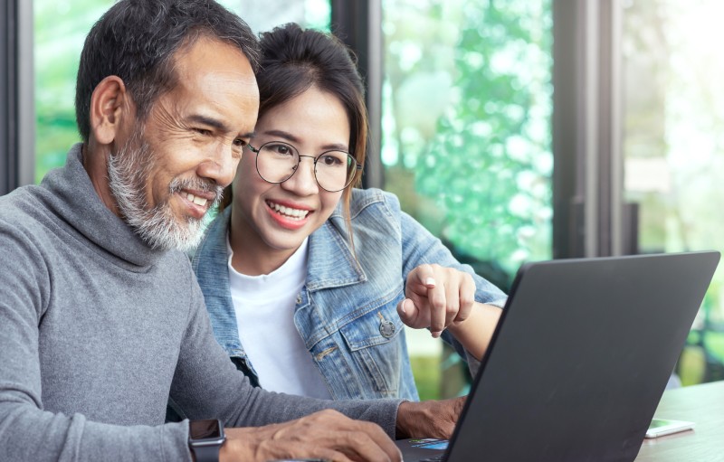 Two adults, one in retirement, comparing AARP dental insurance plans online on a laptop.