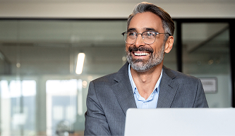 Confident business professional smiling while using a laptop in a modern office, representing broker tools and online resources.