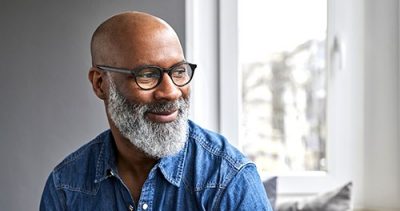 Smiling older man with glasses looking out a window, representing individual dental insurance options.