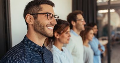Smiling man in a professional setting, standing with colleagues, representing midsize to large group dental insurance options.