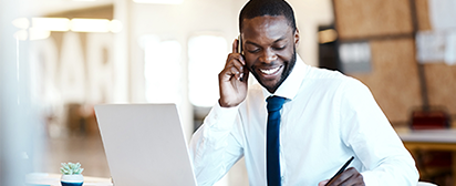 Businessman talking on a mobile phone while working on a laptop, highlighting broker access to digital support tools.
