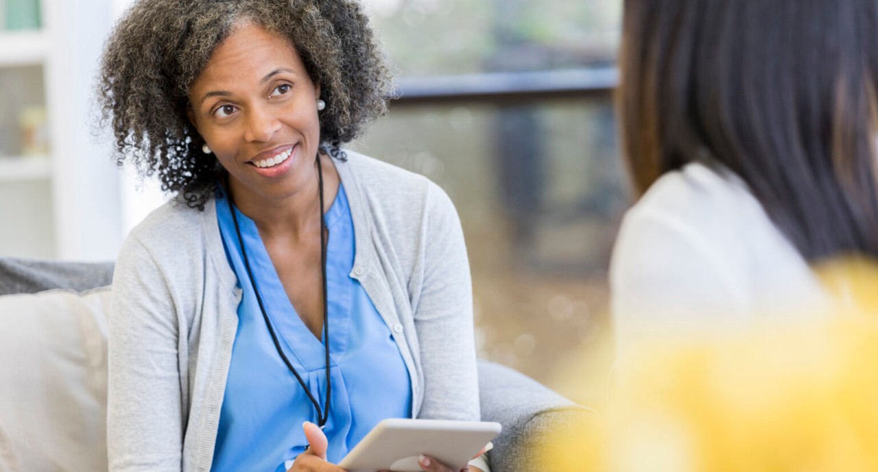 Supportive mature female counselor smiles while listening to a female patient.